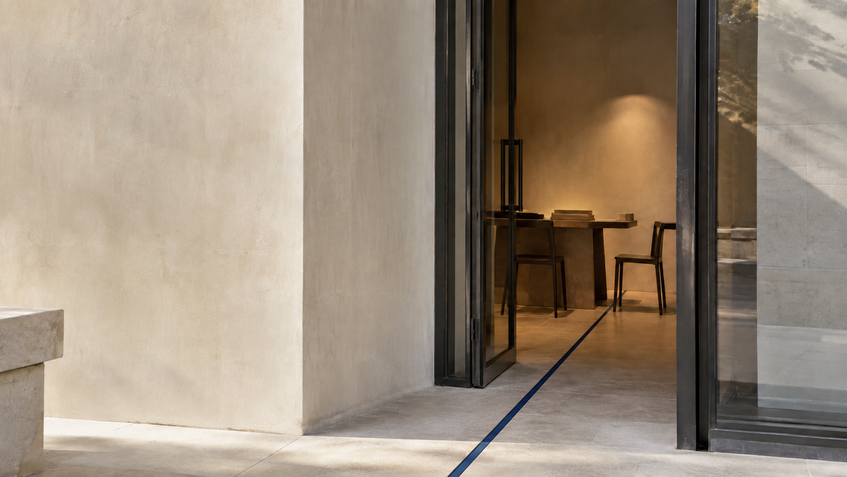A warmly lit studio entrance framed by pale stone walls and dark glass doors